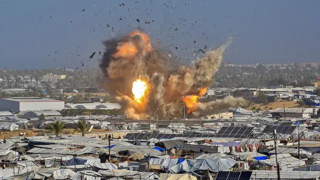 Önde sivillerin kaldığı sıkışık çadır bölgesi ve arkada büyük bir patlama 