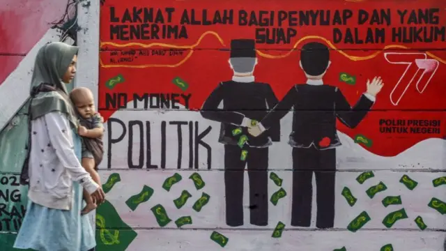 Warga melintas di depan mural yang berisikan tolak politik uang jelang Pemilu tahun 20, di Depok, Jawa Barat, Jumat (28/07).