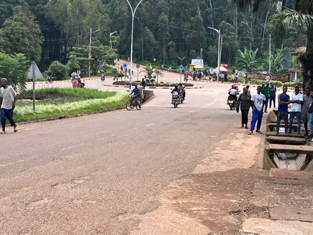 Abantu bahagaze, abarimo kugenda n'amaguru n'abari kuri za moto, mu masangano y'imihanda yo mu gace kazwi nko ku Mukoni, mu mujyi wa Huye, mu majyepfo y'u Rwanda. Ifoto yo ku itariki ya 13 Gicurasi (5) mu 2025.