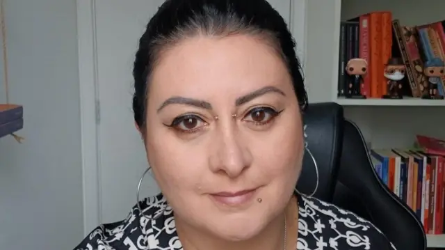 Thaís Basile em escritório, olhando para a câmera com sorriso contido