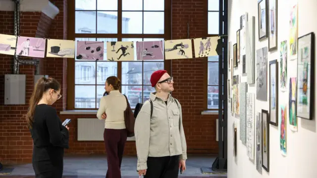 Три человека, две женщины и мужчина, рассматривают картины в арт-галерее