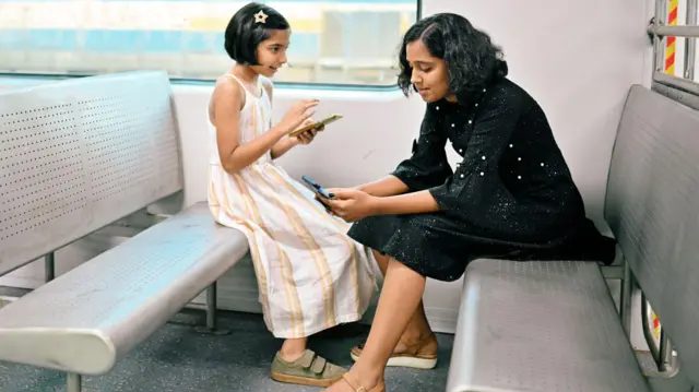 ट्रेन में बैठकर मोबाइल फ़ोन देखती दो लड़कियां