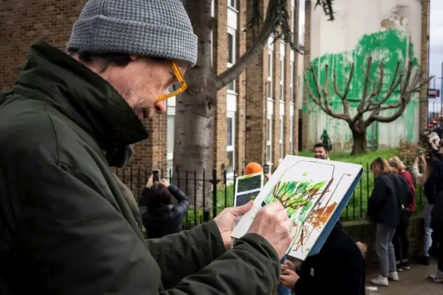 The Banksy mural from further away, where the green paint appears as foliage