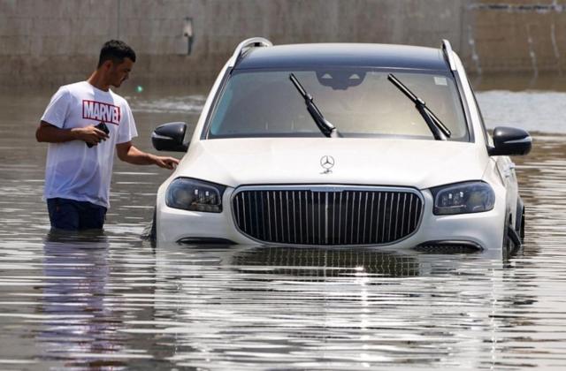 رجل يقف بجوار سيارة غمرتها مياه الفيضانات جزئياً بعد هطول أمطار غزيرة في دبي