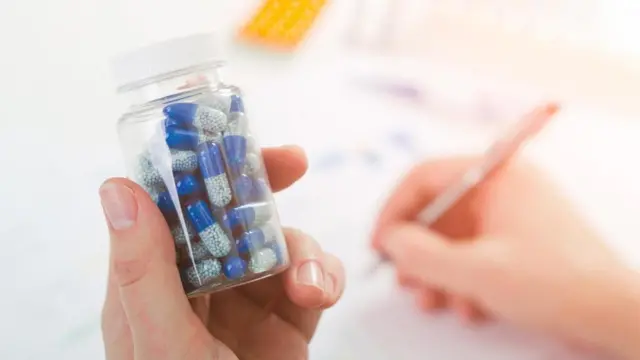 طبيب يكتب بيد، ويمسك بيده الآخرى علبة دواء