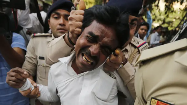 Policía asegurando por las orejas a un manifestante