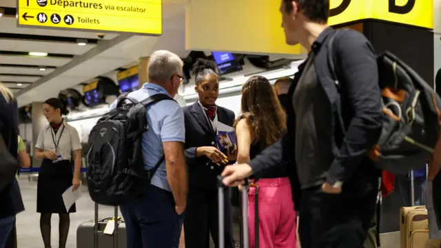 A British Airways staff member speaks to passengers at Heathrow Airport,