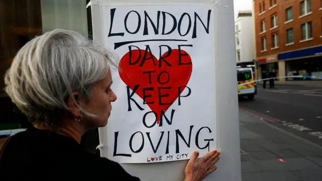 A woman sticks a sign up saying: "London dare to keep on loving"