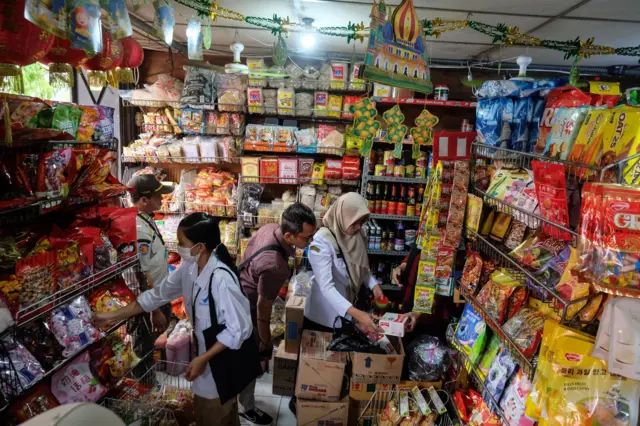 Empat petugas berpakaian dinas sedang memeriksa barang-barang dagangan di sebuah toko.