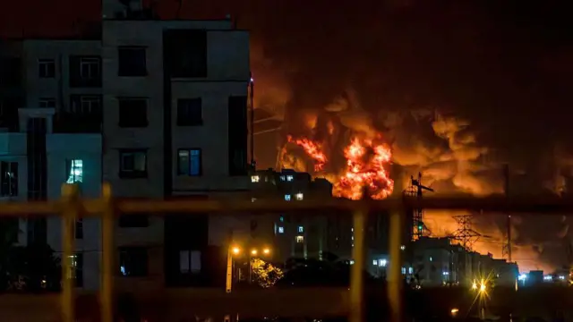 ستونی از دود از محلی که هدف حمله اسرائیل قرار گرفته برخاسته و شعله‌های آتش در شب در تهران دیده می‌شود؛ این تصویر مربوط به سومین روز از موج حملات اسرائیل به ایران در ۱۵ ژوئن ۲۰۲۵ است.