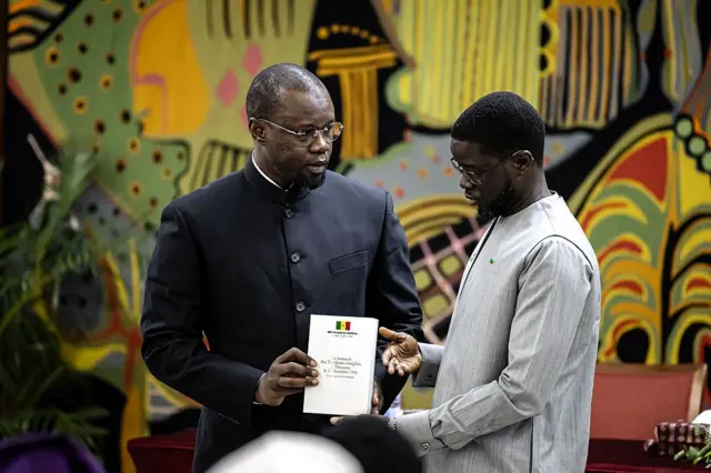 Le Premier ministre sénégalais Ousmane Sonko (à gauche) remet au président sénégalais Bassirou Diomaye Faye (à droite) le rapport officiel sur le massacre de Thiaroye lors d'une cérémonie au palais présidentiel de Dakar, le 16 octobre 2025. 