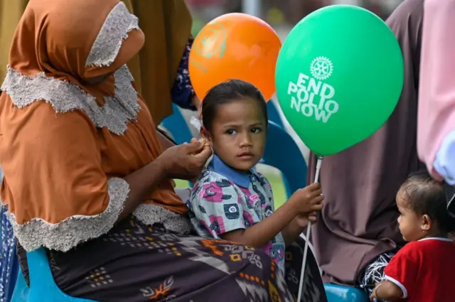 Seorang anak memegang balon bertuliskan 'end polio now'.
