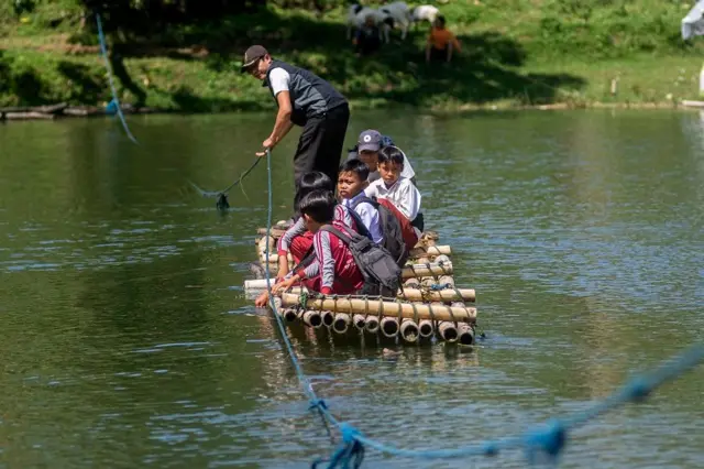 Sejumlah siswa SD menyeberangi Sungai Cicadas menggunakan rakit di Desa Karanganyar, Cililin, Kabupaten Bandung Barat, Jawa Barat, Selasa (27/05).