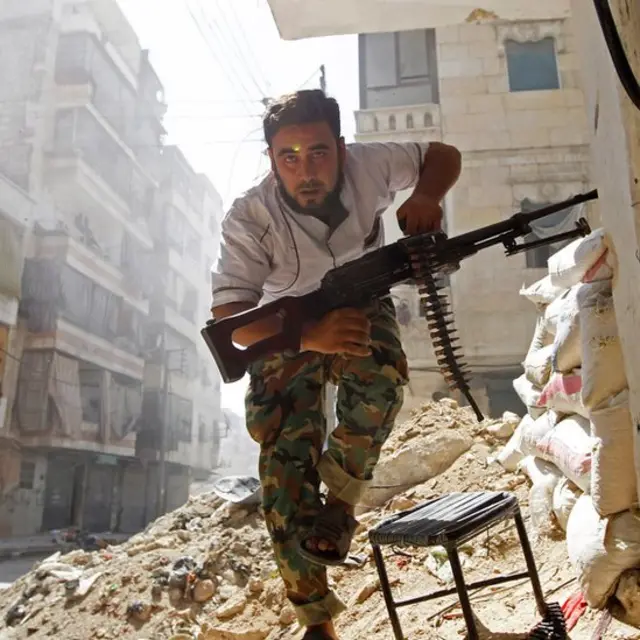 Un hombre armado corre en una destruida Alepo.