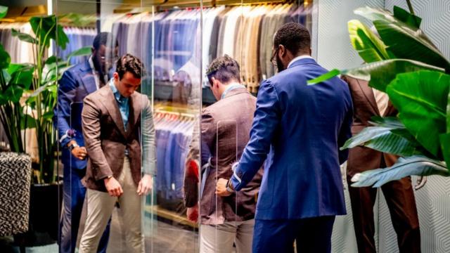 A tailor at Suit-supply in the Netherlands pins a suit on a customer through plexiglass