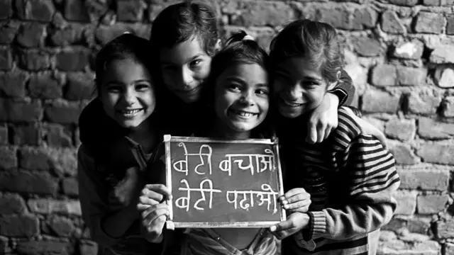 బేటీ బచావో - బేటీ పడావో నినాదం రాసిన పలకను చూపుతున్న నలుగురు బాలికలు