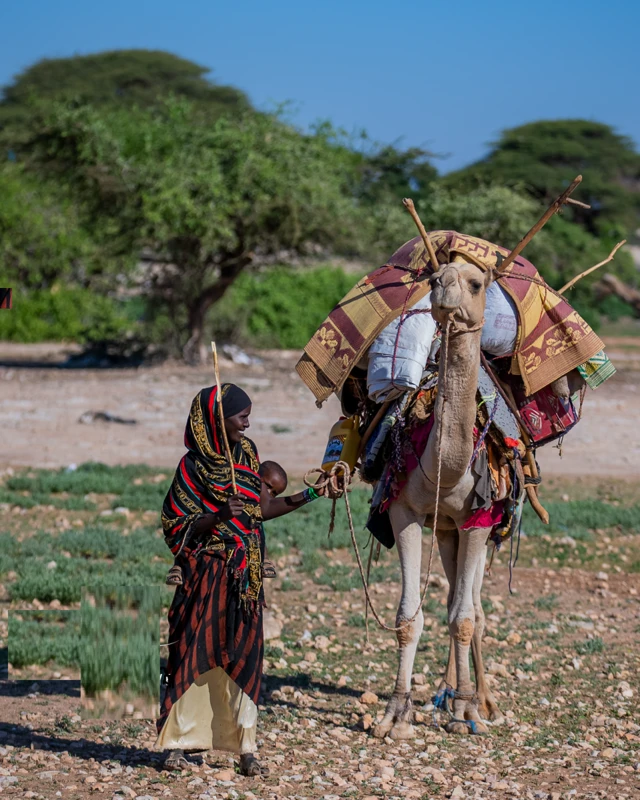 Sawir muujinaya hooyo Soomaaliyeed oo ilmo dhabarka ku sida mayalkana u ahaysa awr ay ku raranyahiin alaabtii reerka oo geedi ah