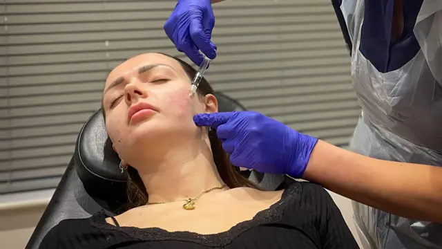 Abby poddaje się zabiegowi zastrzyków w twarz.