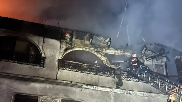 Рятувальник тушить пожежу у пошкодженому будинку