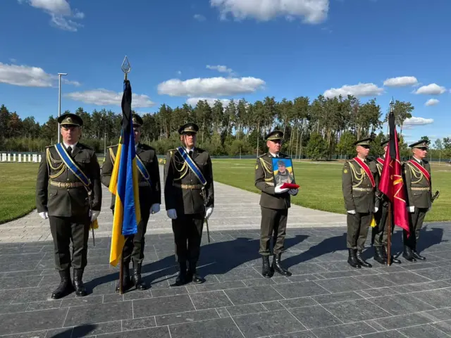 Військові стоять у ряд, один із них тримає портрет військового