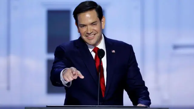 Рубио во время выступления в поддержку Трампа на Республиканской конвенции в июле 2024 года. Он улыбается, стоя на трибуне, и показывает на кого-то пальцем