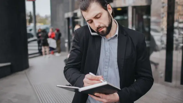 Homem ao celular escrevendofortaleza x sportum caderno enquanto caminha