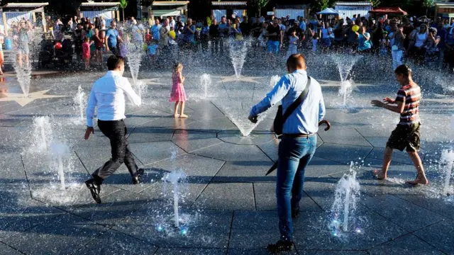 President Volodymyr Zelensky (L) and children refresh themselves in a fountain during his first official visit to Mariupol on 15 June 2019