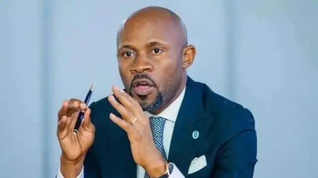 Minisitiri Muyaya mu ikoti ry'umukara n'#ishati yera, afite ikaramu mu kiganza cy'iburyo kandi aragaragara nk'urimo gusobanura ibyo avuga