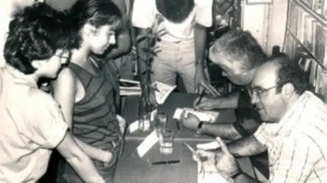 Uğur Mumcu bir imza etkinliğinde sağ tarafında Aziz Nesin ile birlikte okurlarla sohpet ederken. 