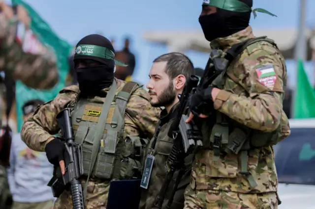 Dos milicianos encapuchados de Hamás armados con fusiles custodian a un rehén en Nuseirat, en Gaza.