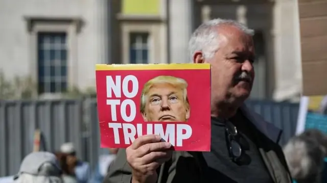 участник акции протеста, у которого в руке плакатик с лицом Трампа и словами "Нет Трампу"