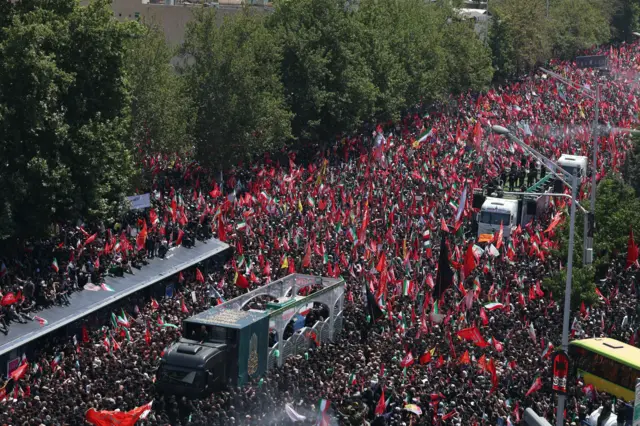 جنازه علی خامنه‌ای در یک لاری قرار دارد و توسط هزاران نفر احاطه شده است. 