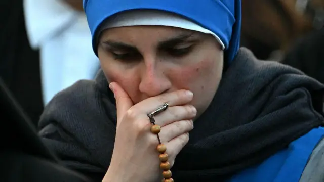 Une femme se tient le visage, avec des perles de prière enroulées autour de ses doigts, alors qu'elle pleure le pape François sur la place Saint-Pierre après l'annonce de sa mort, le 21 avril 2025.