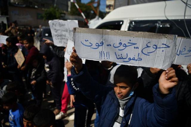 أطفال فلسطينيون نازحون في رفح يتظاهرون دعماً لأقرانهم الذين يتعرضون لمجاعة أكبر شمال غزة، بتاريخ 21 فبراير/شباط 2024