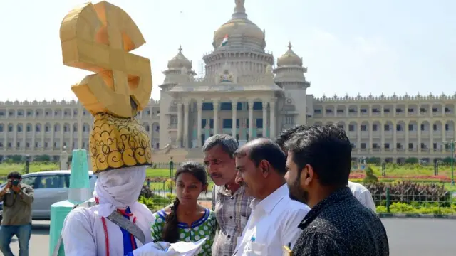 कर्नाटक विधानसभेसमोर निवडणूक आयोगाचं चिन्ह घालून मतदानासाठी आवाहन करणारा माणूस.