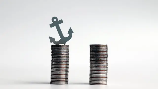 Ancla en miniatura sobre dos pilas de monedas.