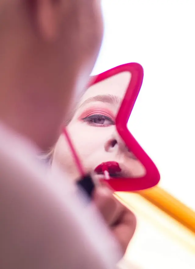 Una mujer prepara su maquillaje frente al espejo.
