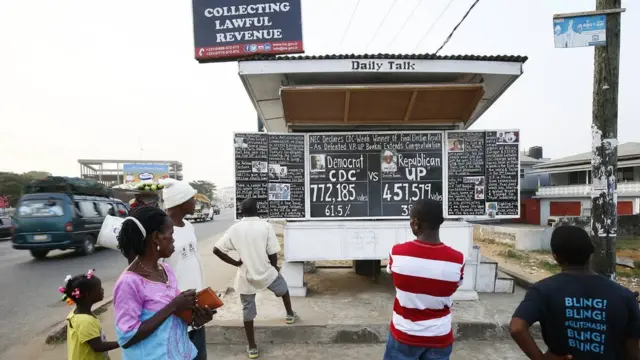 أشخاص ينظرون إلى لوحة بها أرقام لنتائج الانتخابات في ليبيريا