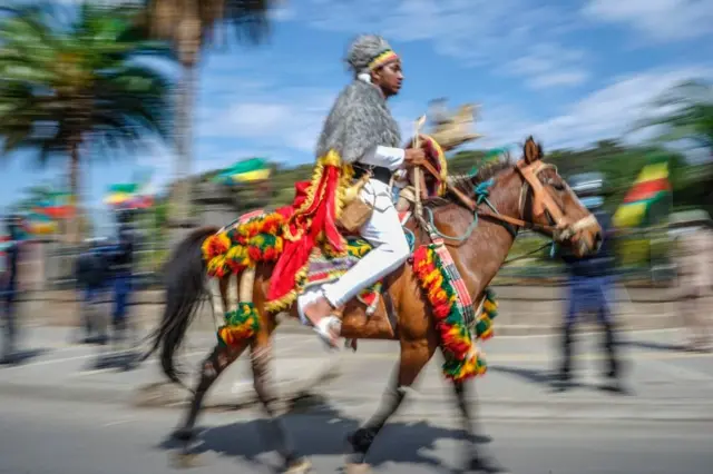 A man is seen riding a horse. Bother are wearing green, yellow and red colours for their symbolism.