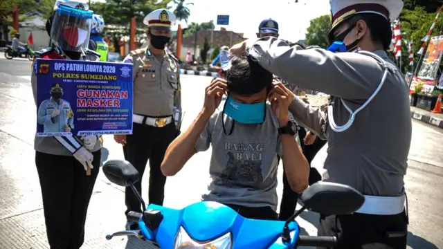 Petugas mengenakan masker kepada seorang pengguna kendaraan saat Operasi Patuh Lodaya di Bunderan Binokasih, Kabupaten Sumedang, Jawa Barat, Sabtu (25/07).
