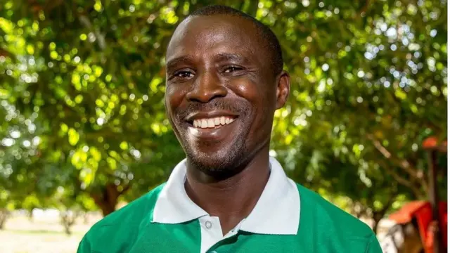 Young wey wear N-Power T-Shirt man dey smile