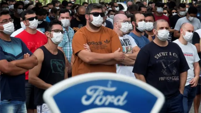 Dezenassite de apostas mais segurohomens e mulheressite de apostas mais seguromáscaras e braços cruzados durante protesto, com logo da Ford na frente destas pessoas