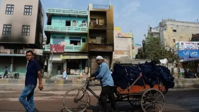 ਸੜੇ ਹੋਏ ਘਰਾਂ ਸਾਹਮਣਿਓਂ ਲੰਘ ਰਹੇ ਦੋ ਲੋਕ