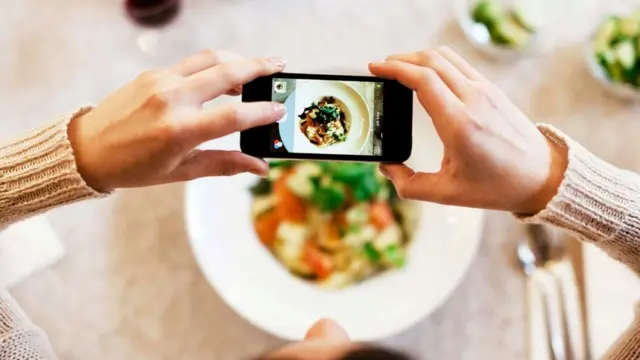 Una mujer tomando una foto a un plato de comida con su teléfono