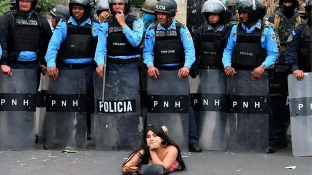 Seorang pengunjuk rasa berbaring di jalan di depan petugas polisi selama demonstrasi menentang pemilihan ulang Presiden Hernandez yang diperebutkan di Honduras