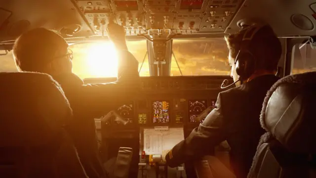 Piloto y copiloto en un avión durante la puesta de sol.