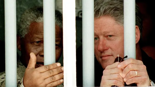 March 27, 1998 US President Bill Clinton (R) and South African President Nelson Mandela look out the jail cell window 27 March where Mandela spent 18 of his 27 years as a political prisioner on Robben Island.