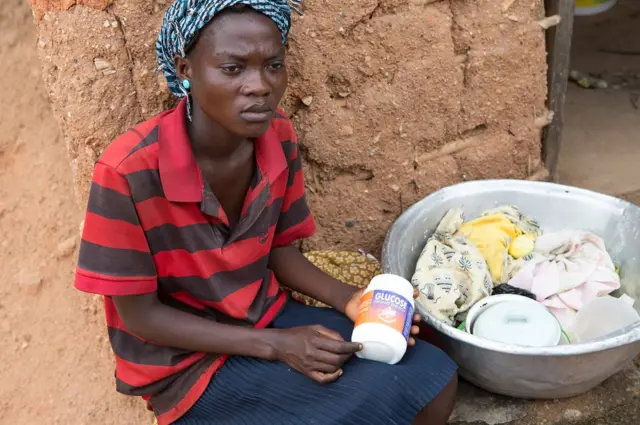 Mary Essil sits outside her home holding a bottle of glucose