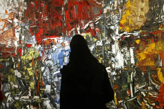 بازدید کننده‌ ایرانی مقابل تابلویی از ژان پل ریوپله ایستاده است