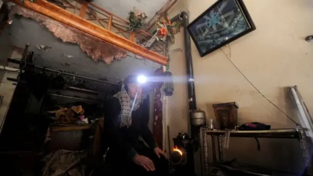 Hombre sentado en su casa abrigado con una linterna en Alepo, Siria.